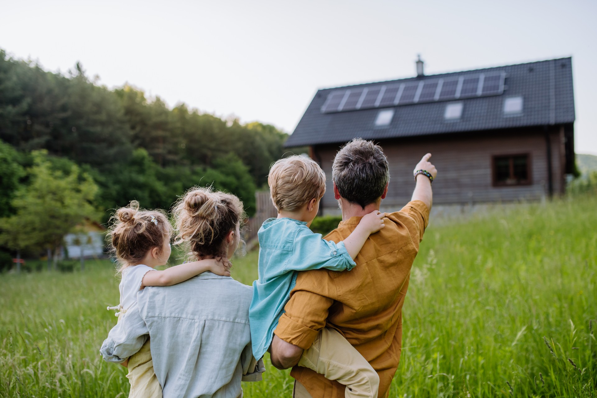 Glückliche Familie vor ihrem Haus mit Sonnenkollektoren auf dem Dach.